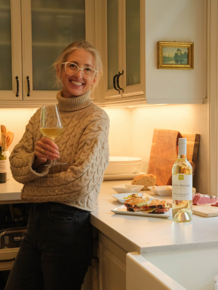 Nicole smiling holding a glass of sauvignon blanc and corned beef sandwich
